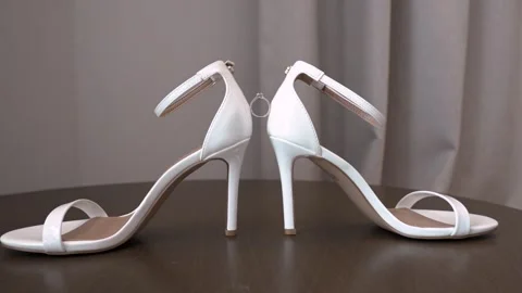 White high heel sandals display on a wooden table in a simple indoor setting Stock Footage 335995932