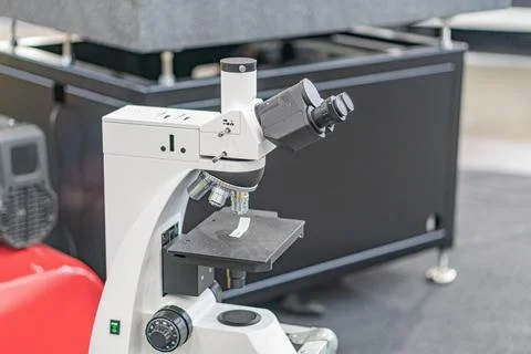 A white, high-powered optical microscope on a movable base in a laboratory se Stock Photos