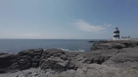 White historic lighthouse standing on rugged rocky coast in ireland Stock Footage 340456309