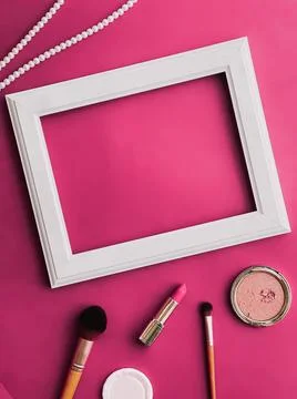 White horizontal art frame, make-up products and pearl jewellery on pink back Stock Photos