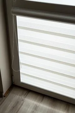 White horizontal blinds partially open in a modern interior, creating layered Stock Photos