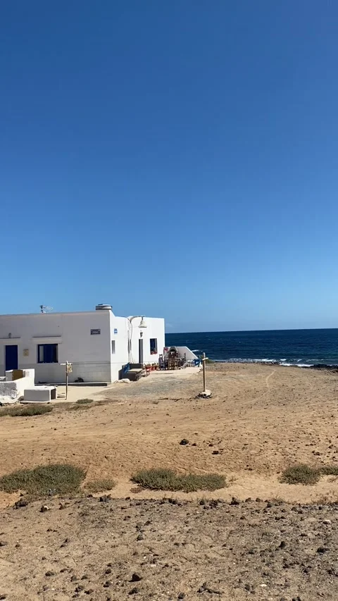 White house with blue windows facing the ocean in Caleta de Sebo La Graciosa Stock Footage 310607402