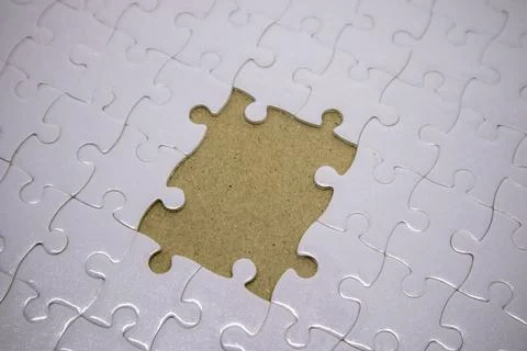 A white jigsaw puzzle with a large missing piece in the center revealing ca.. Fotos de archivo