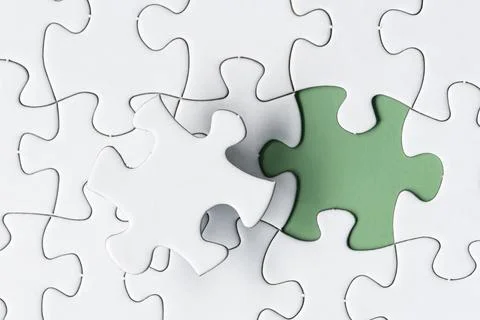 White jigsaw puzzle with missing piece on green background. Copy space. Stock Photos