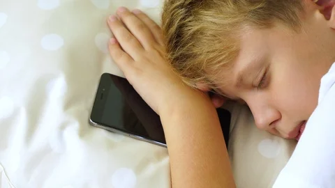 White kid sleeping in his bed with black modern smartphone in hand. Stock Footage 94222736