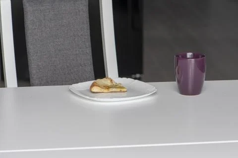 On the white kitchen table are leftovers, a mug, and a slice of pizza on a pl Fotos Stock