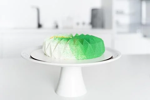 In the white kitchen on the table there is a green mousse cake Stock Photos
