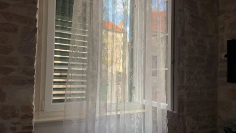 White lace curtains blowing in the breeze at an open window with stone wall Stock Footage 341663158