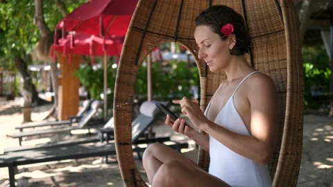 White lady using her phone while swinging in a cocoon chair.Staying connected on Stock Footage 159968718