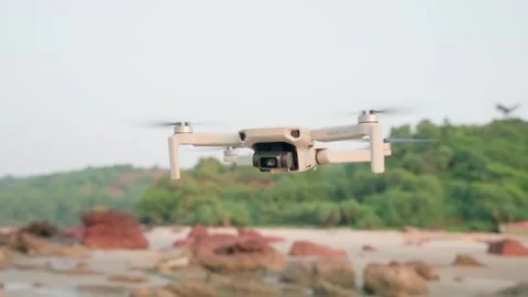 A white large quadrocopter hangs on the shore, the blades spin quickly. Video stock 228684844