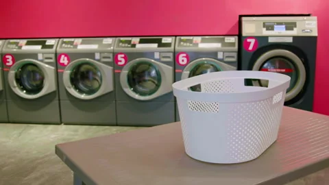 White laundry basket placed on a table in a self-service laundromat with washing Stock Footage 328105732