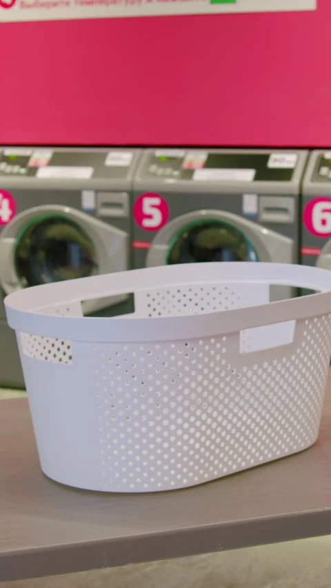 White laundry basket placed on a table in a modern laundromat, with washing Stock Footage 330020411