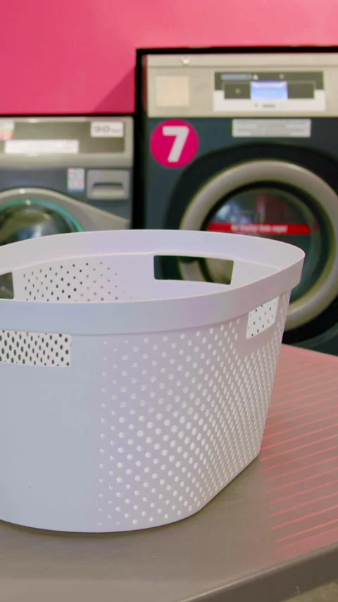 White laundry basket placed on a table in a laundromat with washing machines and Stock Footage 330020448