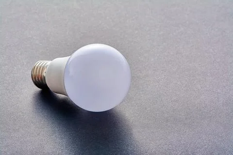 A white LED lamp with an E27 base lies on a gray background Stock Photos