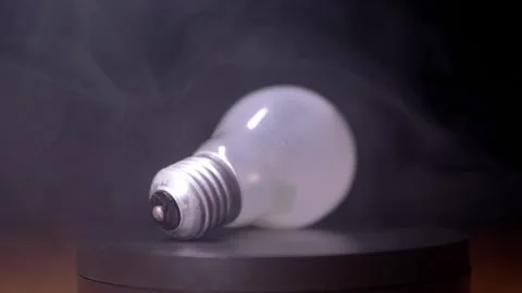 White Light Bulb Lying On Side Surrounded By Thick Smoke On Dark Background 库存影片 330113777