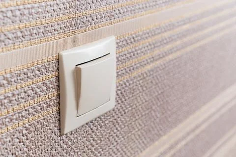 White light switch on the wall with brown wallpaper. Stock Photos