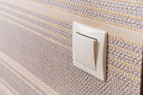 White light switch on the wall with brown wallpaper. Stock Photos