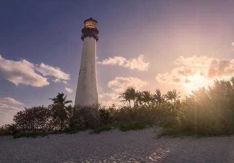 A white lighthouse against deep blue sky with setting sun tinting white clouds Stock Photos