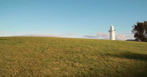 White lighthouse appears over green hill at sunset Stock Footage 137766639