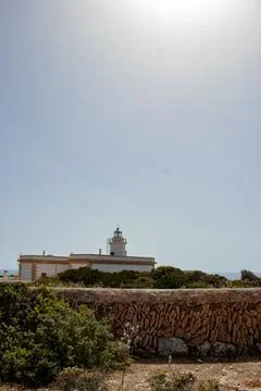 White Lighthouse Atop Mountain Overlooking Clear Blue Sea Foto stock