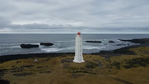 A white lighthouse on a black sand beach in cloudy weather Stock Footage 226575960