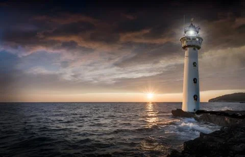 White Lighthouse on Coastal Rocks at Dramatic Sunset Stock Photos