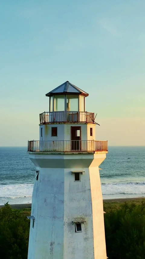 White lighthouse overlooking blue sea at dusk Vídeo Stock 335432627