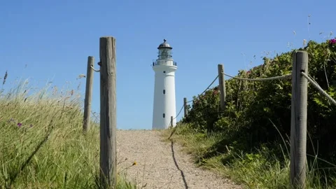 White lighthouse standing on coastal sand dune path Stock-Footage 338329286