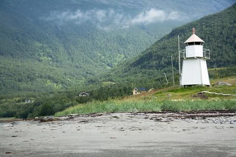 White lighthouse standing on sandy beach in norway with green mountains Stock Photos
