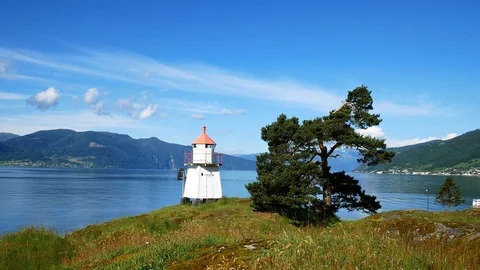 White lighthouse tower with red top and nearby evergreen tree along fjord. Stock Footage 120397488