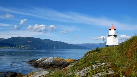 White lighthouse tower with red top and moss covered rocky shore in Norway. Stock Footage 120398172