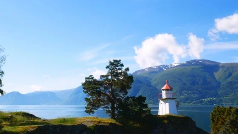 White lighthouse tower with red top and nearby fir tree along a fjord. Stock Footage 120749741