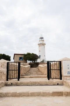 White lighthouse under a partly cloudy sky surrounded by trees Stock Photos