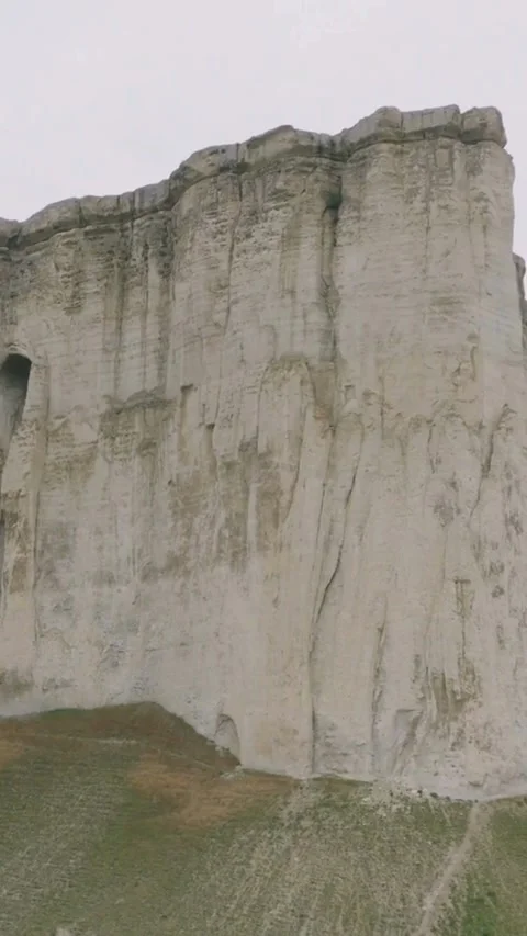 White limestone cliff face with cave stands above grass Video stock 334168930