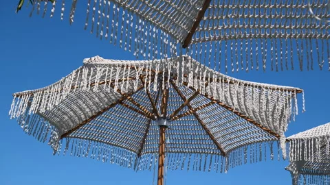 White macrame beach umbrella with fringe against clear blue sky at summer resort 库存影片 343441107