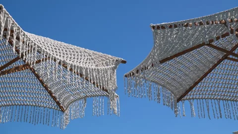 White macrame beach umbrellas against a clear blue sky on a sunny day 스톡 동영상 343441284