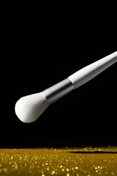 White makeup brush on a dark background. Scattered golden sequins. Stock Photos