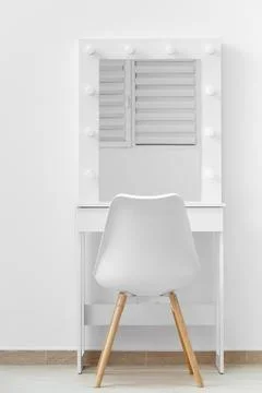 White makeup dressing table with lamps and a chair against a white wall Stock Photos