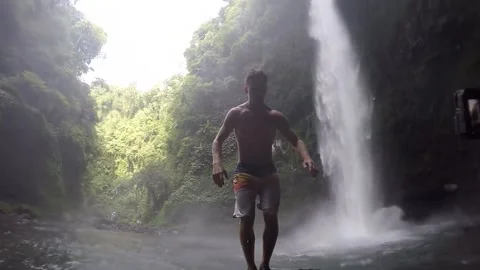 A white male does a backflip into a pool of water underneath a massive waterfall Stock Footage 146628193