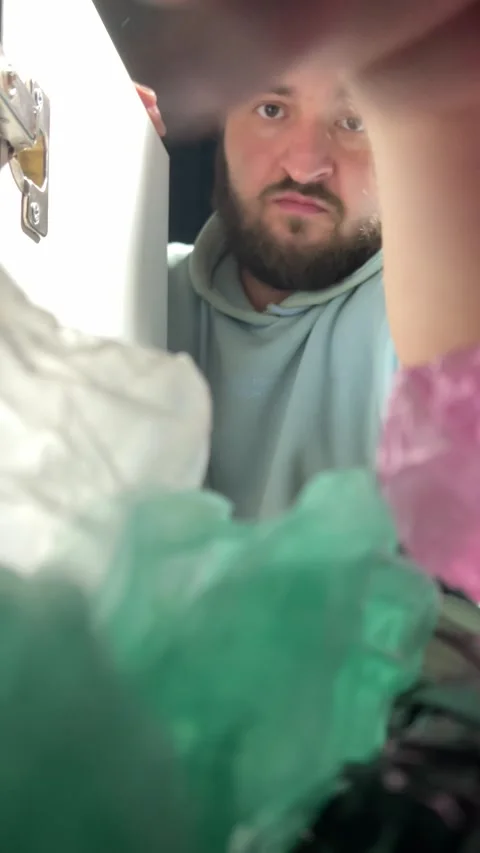 White man with beard puts black plastic cellophane bag on shelf in closet Stock Footage 297210286