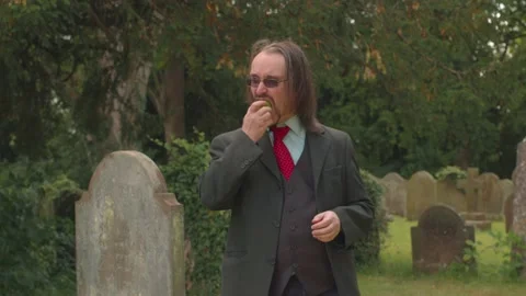 White Man With Beard In Suit Eats Apple In Graveyard Video stock 138675842
