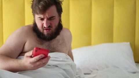 White man with beard wakes up in yellow hotel bed room, reads sms Stock Footage 314505885