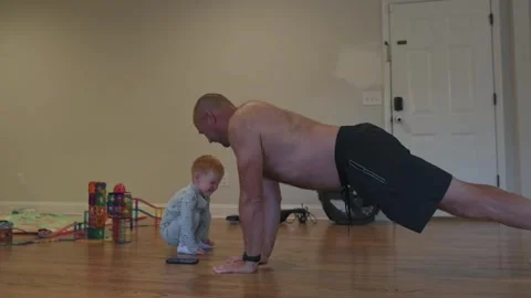 White man doing push-ups with baby on hardwood floor, focused home workout near Vídeo Stock 323092203