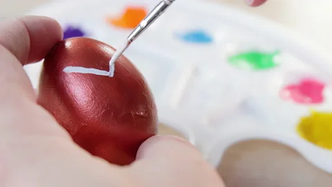 A white man drawing white lines with a brush on a copper colored Easter egg Stock Footage 172142920