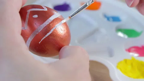 A white man drawing white lines with a brush on a copper coloured Easter egg Stock Footage 172330927