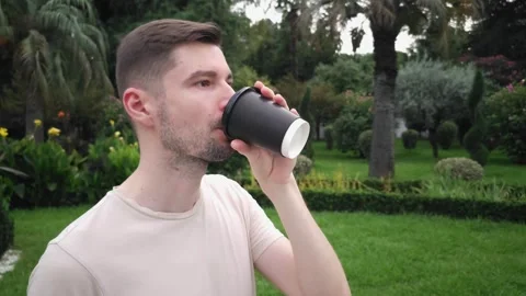 White man drinking coffee from black disposable cup in a park Stock Footage 283404159