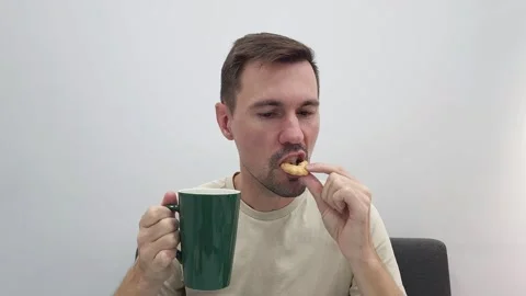 White man eating a cookie while holding a green cup of coffee or tea Stock Footage 282610845