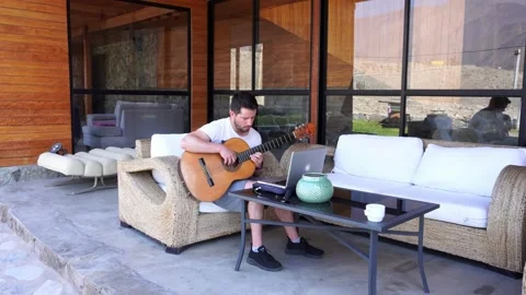 A white man giving virtual music classes with his laptop and guitar in a country Stock Footage 199510096