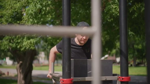 White Man Performing Dips On Parallel Bars In Sunny Park, Focused Downward Gaze Stock-Footage 324754880