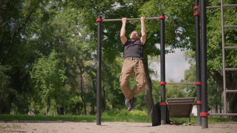 White Man Performing Intense Pullup Repetitions On Outdoor Bars Legs Tucked Stock Footage 327167596
